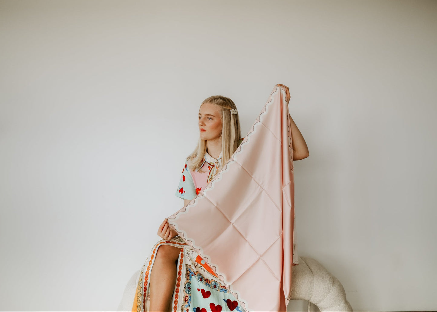 Woman holding a pale pink scarf against a plain background