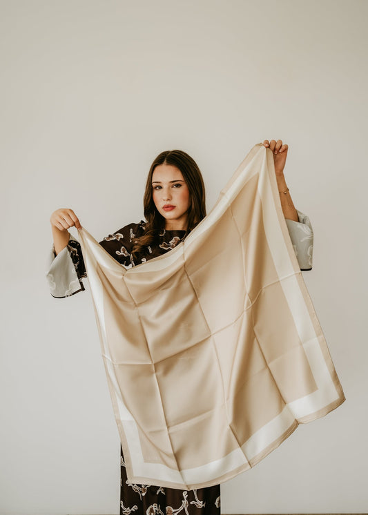 Woman holding a beige silk scarf against a plain background