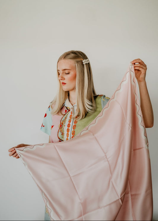 Woman holding a pale pink scarf against a plain background